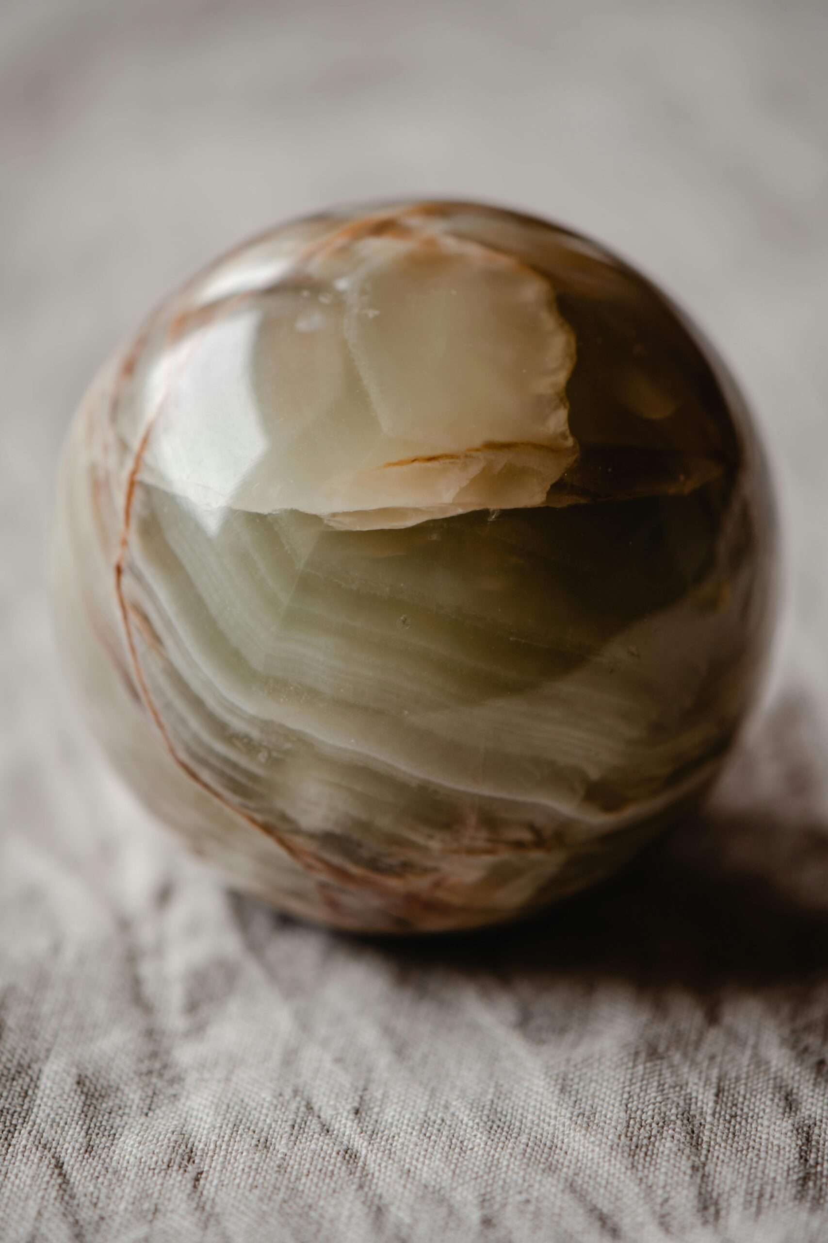 Close-up of a polished onyx sphere showcasing intricate natural patterns and earthy tones against a textured fabric background.